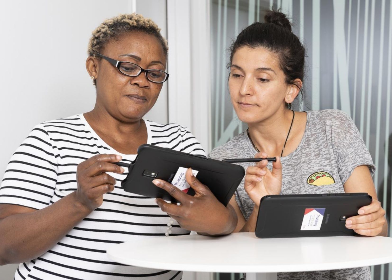 2 dames die op hun mobiel werken met de zorg@home app